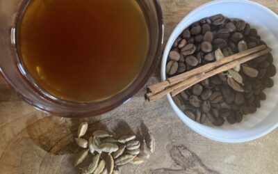 un vaso con café sobre una mesa de madera junto a semillas de cardamomo granos de café Y un palo de canela