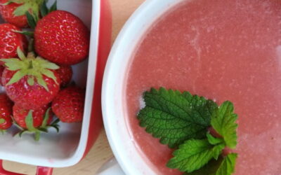 desde arriba una taza de gazpacho conuna ramita de hierbabuena y al lado un cuenquito con fresas