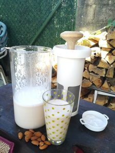 receta de leche de almendras concentrada leche de almendras concentrada en un recipiente junto a un vaso de leche y el filtro de vegan milker al fondo